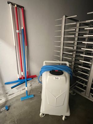 une valise blanche avec une poignée bleue, posée à côté d'un support sur lequel sont accrochés des tuyaux rouges et bleus