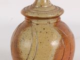 un petit vase muni d'un couvercle, posé sur une surface blanche