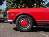 a red car parked in a parking lot with a tree in the background