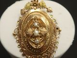 a close up of a gold plated pendant on a white stand
