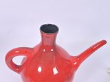 a red vase with a black handle on a white table