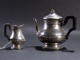 a silver tea pot and a silver cup on a table