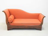 un canapé orange posé sur un sol blanc, à côté d'un mur blanc