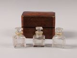 three small glass bottles sitting next to a wooden box on a white surface