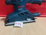 une ponceuse orbitale Bosch posée sur une table, à côté d'une boîte rouge