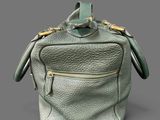 green leather handbag on grey background with gold handles