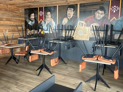 de nombreuses chaises et tables dans un restaurant où est accrochée une peinture au mur
