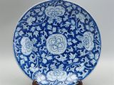 assiette bleue et blanche ornée de fleurs et de rinceaux, posée sur un socle en bois