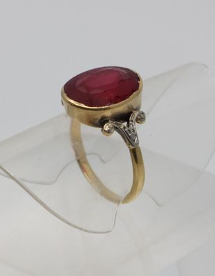 une image représentant une bague ornée d'une pierre rouge posée sur un morceau de verre transparent