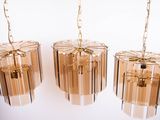 three glass chandeliers hanging from a gold chain on a white wall