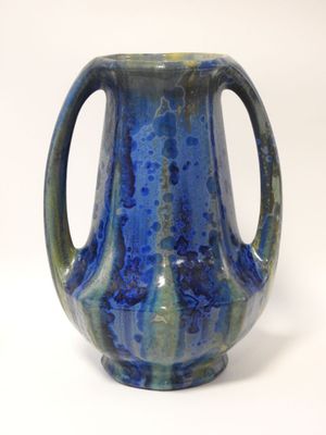 un vase bleu muni d'une anse, posé sur une surface blanche