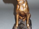 bronze statue of a dog sitting on a rock on a gray surface