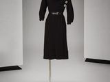 une robe noire avec des boutons et une ceinture, posée sur un présentoir pour mannequin