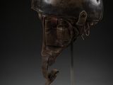 a bronze helmet on a metal stand with a black background