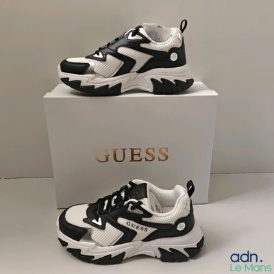 deux paires de baskets noires et blanches exposées devant une boîte blanche