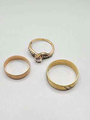 three gold rings and a diamond ring on a white surface