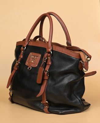 un sac à main en cuir noir et marron posé sur une table à côté d'une tasse de café