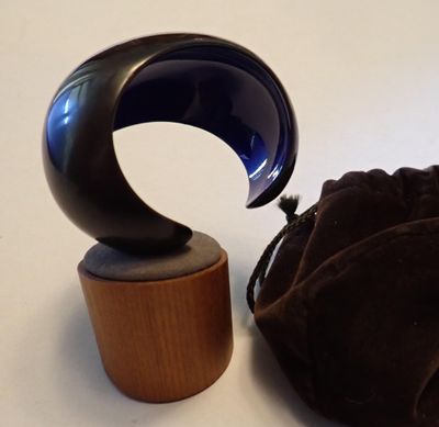 un objet en verre bleu posé sur un socle en bois, à côté d'un sac noir