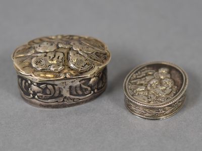 deux bijoux en argent et en or posés l'un à côté de l'autre sur une surface grise