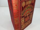 an old book with a red cover sitting on top of a white table
