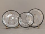 three clear glass plates with gold rims on stands against a white background