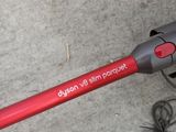 a red corded vacuum on the floor next to a charger