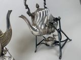 a silver tea pot and a silver tea kettle on a stand