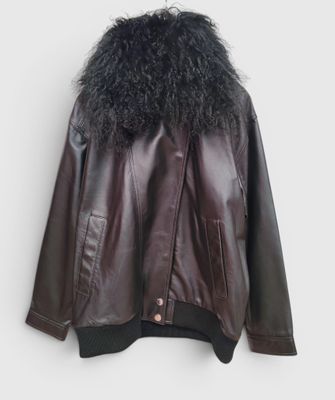 une veste en cuir marron avec un col en fourrure noire, suspendue à un cintre devant un mur blanc