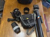 une table sur laquelle sont posés un appareil photo, un sac pour appareil photo, un trépied, un appareil photo et un objectif