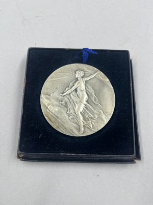 une image représentant une médaille d'argent ornée d'un ruban bleu, posée sur un coffret noir