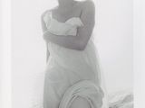 une vieille photo d'une femme en robe blanche, assise sur un lit