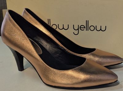 Les chaussures dorées sont posées sur une surface blanche, avec une boîte en arrière-plan.