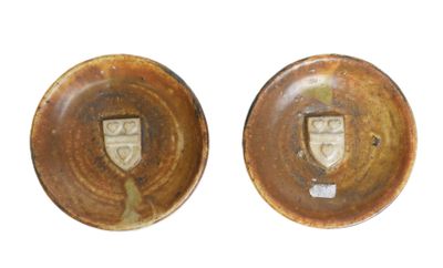 two brown pottery plates with a crest on them on a white surface
