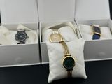 three watches in a white box with a gold chain around the strap