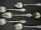 six cuillères en argent sont alignées sur une surface noire
