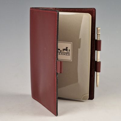un livre rouge contenant un stylo, avec un bloc-notes posé devant