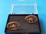 une paire de bracelets manchette dorés, présentés dans un coffret noir posé sur un fond bleu