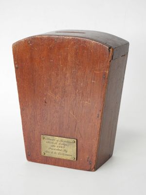 une vieille boîte en bois ornée d'une plaque, posée sur une surface blanche