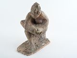 statue of a man sitting on a tree stump with his hands on his knees