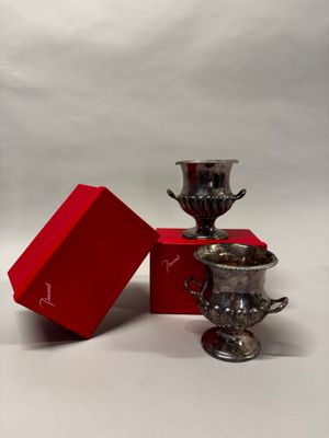 deux tasses en argent posées à côté d'une boîte rouge sur une surface blanche