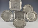 six plats et plateaux en métal argenté posés sur des supports, disposés sur une surface blanche