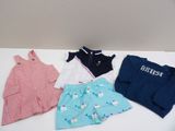 Trois paires de vêtements pour bébé sont posées sur une table blanche.