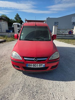 La voiture rouge est garée sur la terre battue du parking.