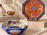 an orange and blue bowl sitting on top of a table next to a lamp