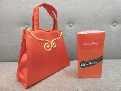 un sac à main orange posé à côté d'un coffret de parfum sur un canapé