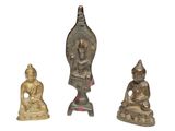 trois petites figurines de Bouddha en bronze posées sur une surface blanche