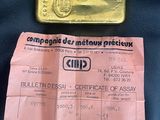 un lingot d'or et un certificat posés sur un sac en cuir noir, sur une table