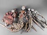five antique dolls are lined up in a row on a gray surface