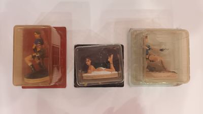 three miniature figurines of a woman laying on a bed in a box