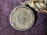 a silver coin with a chain around it on a purple surface